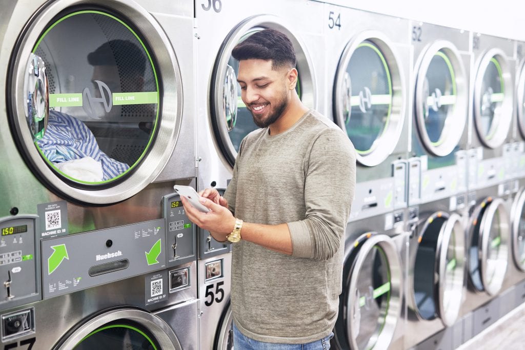 man smiling at his phone at a Huebsch laundromat