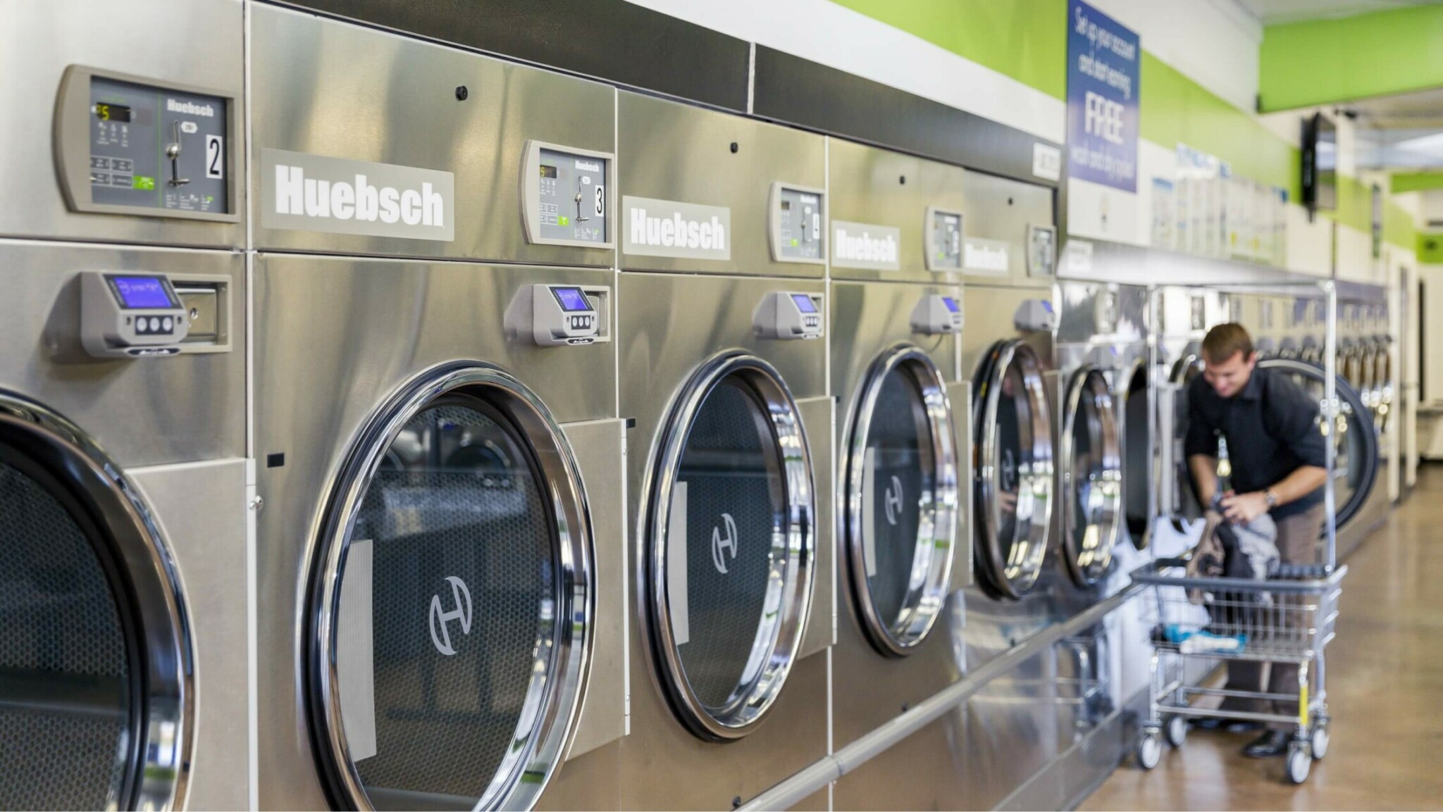 man standing with cart in front of row of washing machines